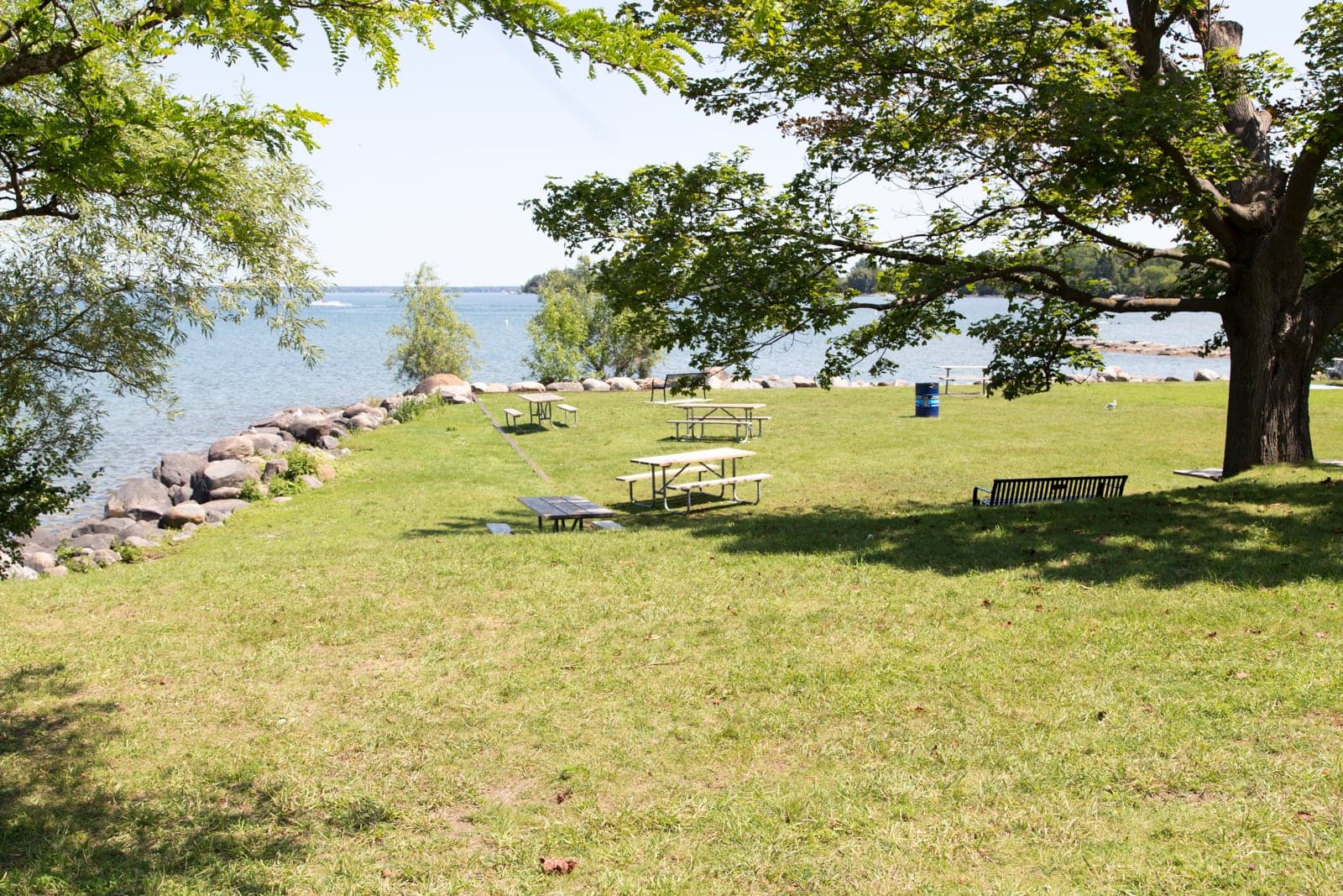 A quiet, rocky stretch of shoreline and picnic tables under shade trees at De La Salle Park