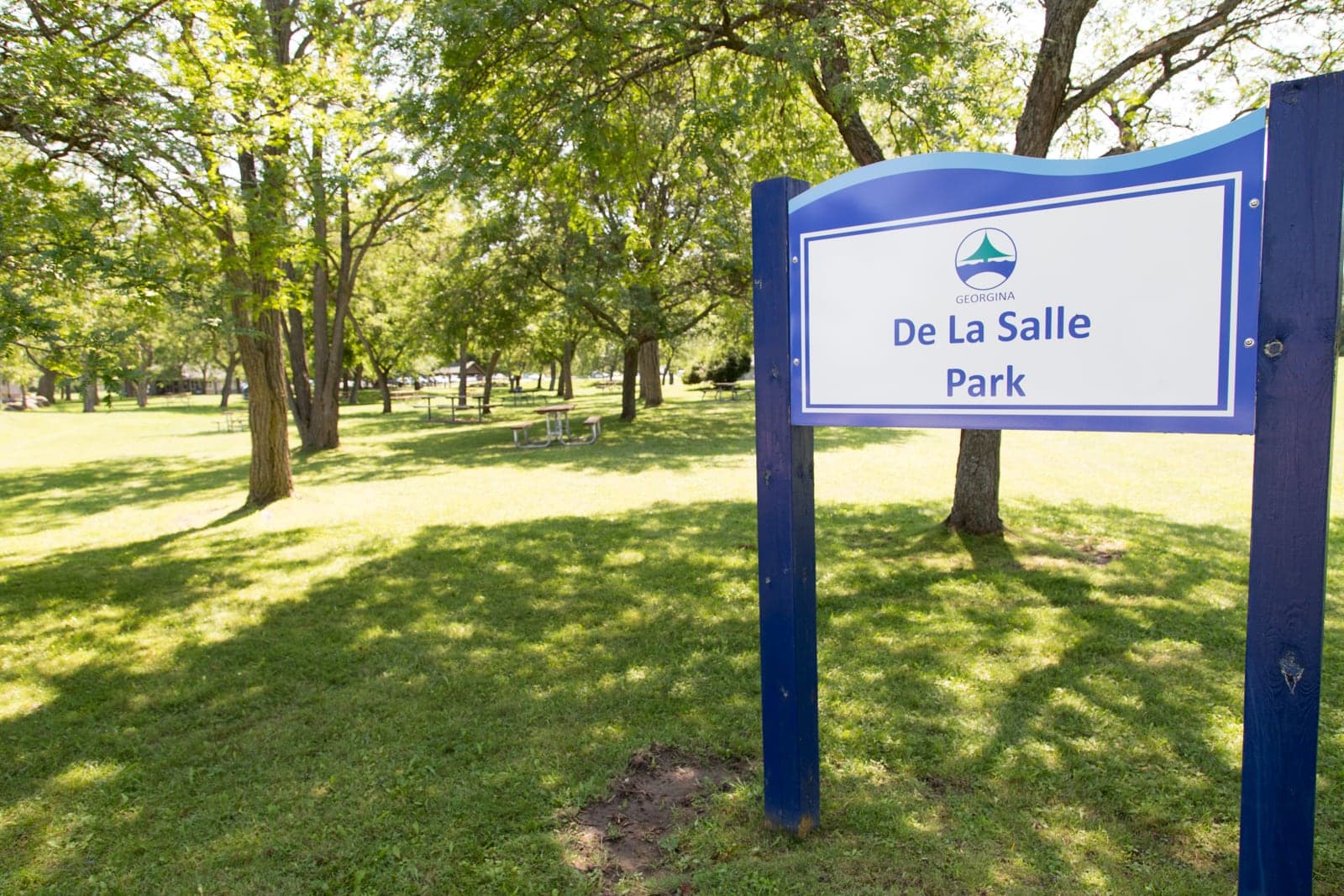 The De La Salle Park sign, with picnic tables and shade trees behind it