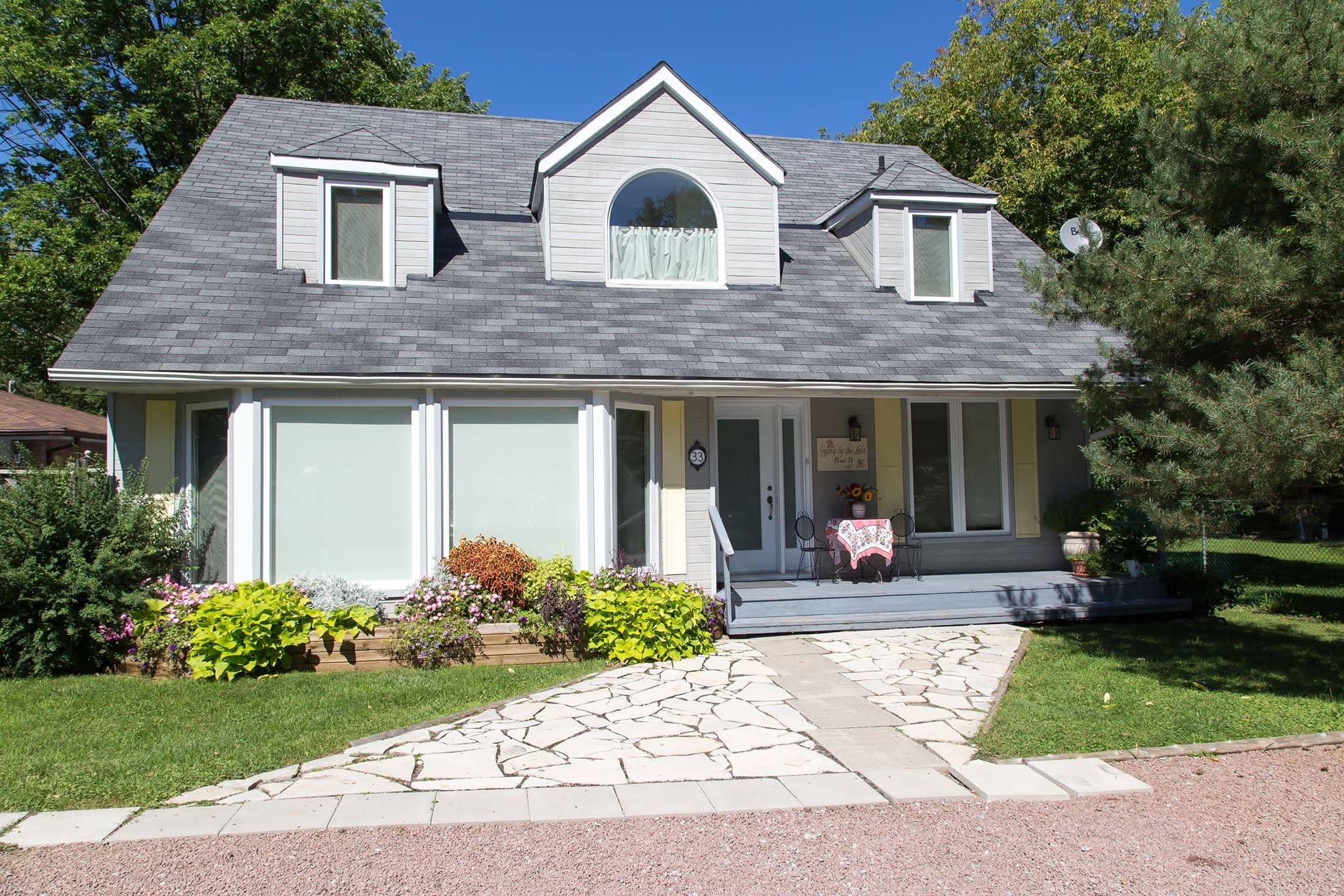 Gypsy by The Lake, a grey cottage with white dormer windows and a flagstone path, on a clear summer morning