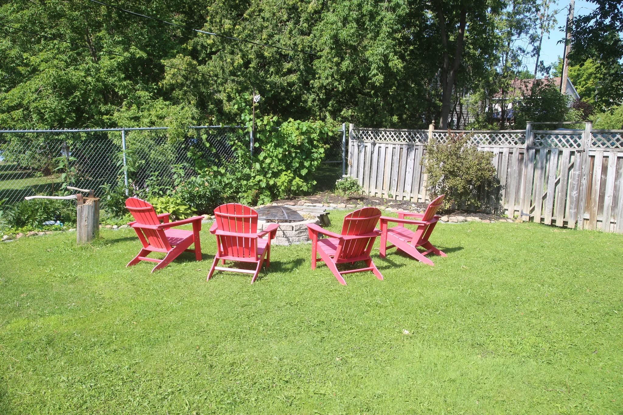 Four red Muskoka chairs gathered around the stone fire pit on the back lawn