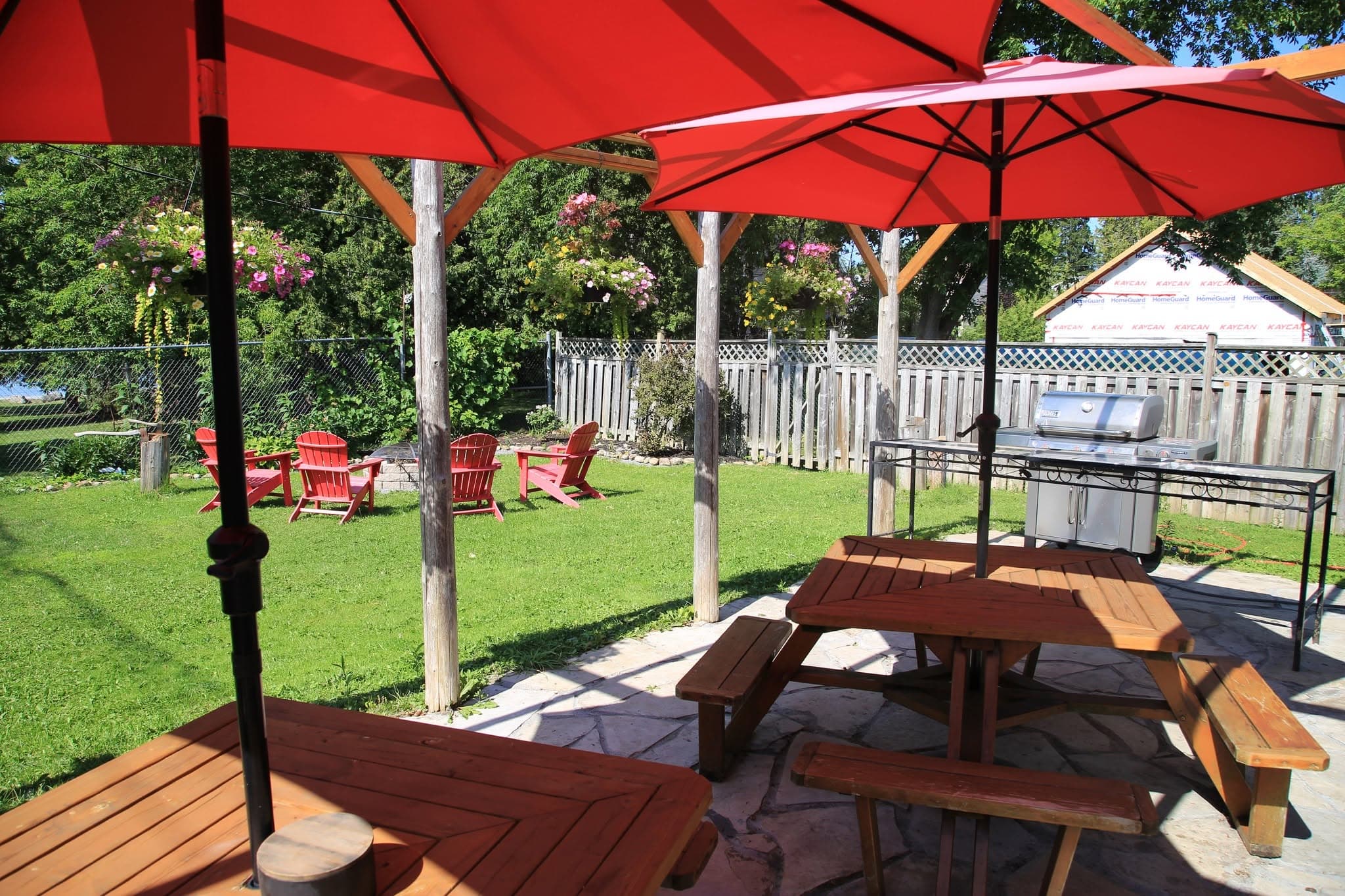 Two cedar picnic tables under red umbrellas, with the fire pit and lawn beyond
