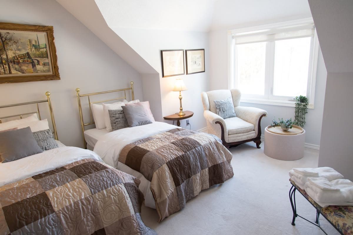Two brass bedsteads with patchwork quilts and a wingback armchair by the window