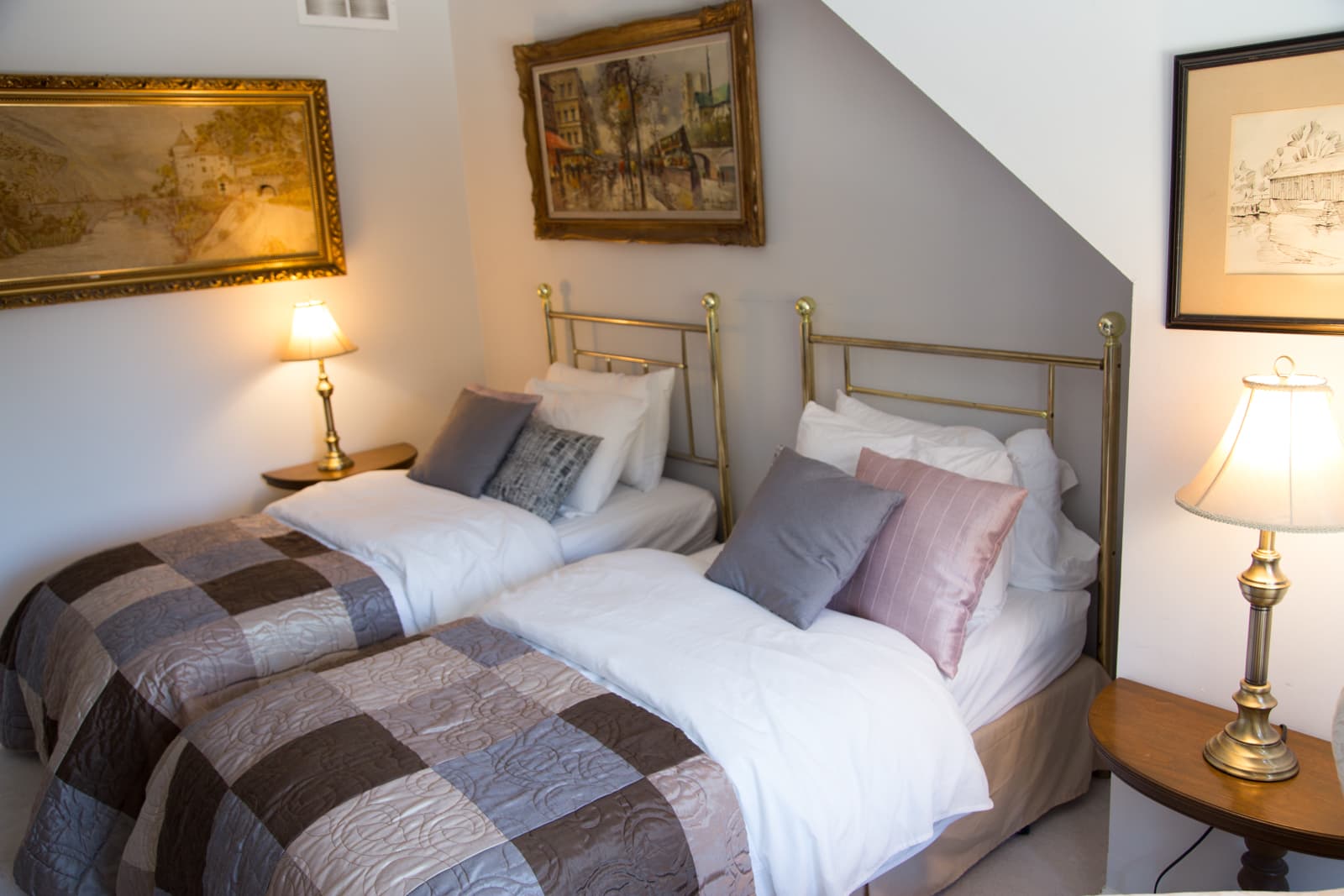 Two brass bedsteads with patchwork quilts and mixed grey, blush and pink cushions