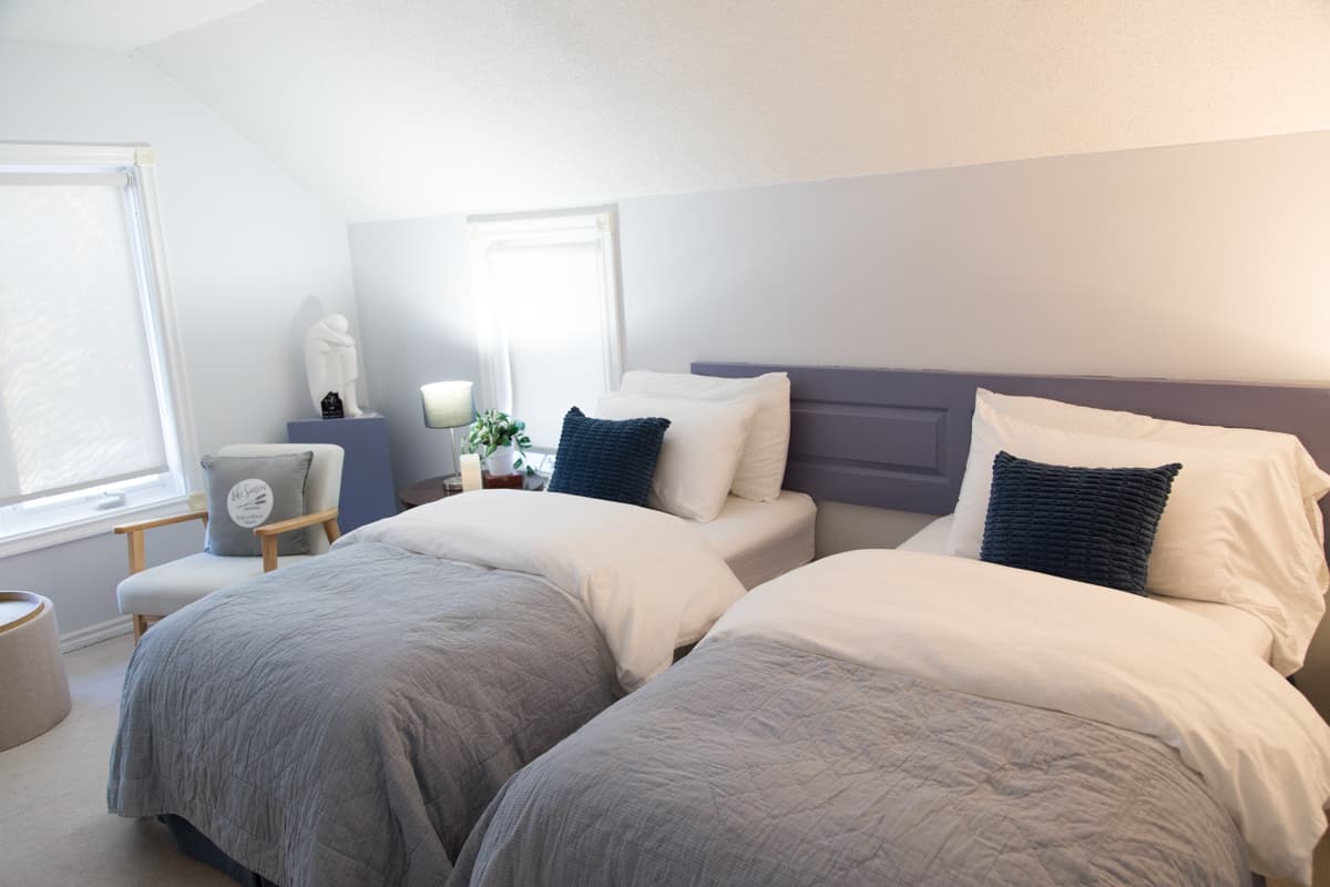 The same room set up with two twin beds under soft grey quilts and navy cushions